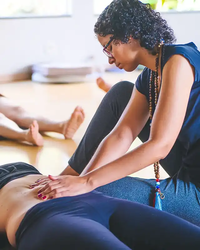 Facilitadora concentrada aplica toque somático no abdômen de aluna para ativar pontos marmas no Curso de Ativação da Kundalini.