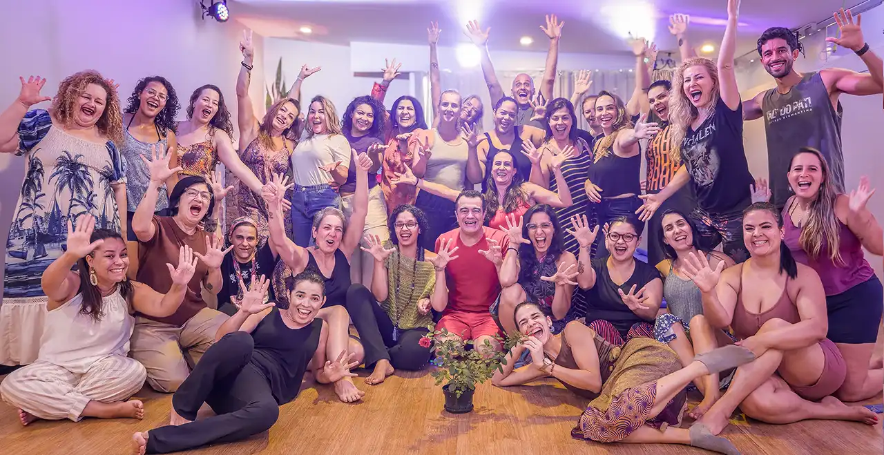 Turma do curso de Massagem Somática sorrindo com as mãos espalmadas junto ao professor Fábio Nirvano.